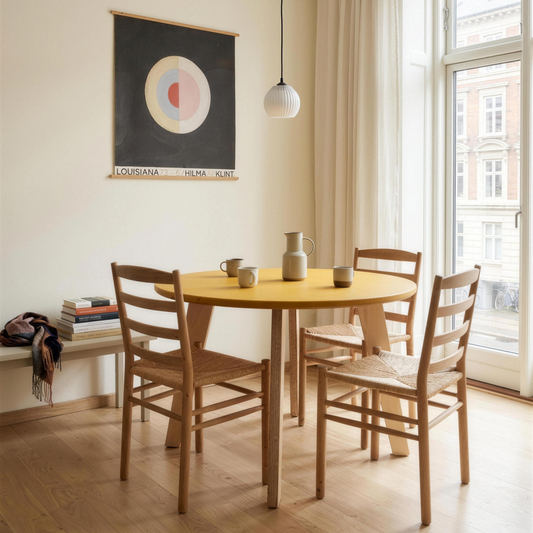 Mesa de comedor redonda Bjørk en Valchromat® amarillo con patas de contrachapado de abedul, junto a una ventana alta en un apartamento de Copenhague