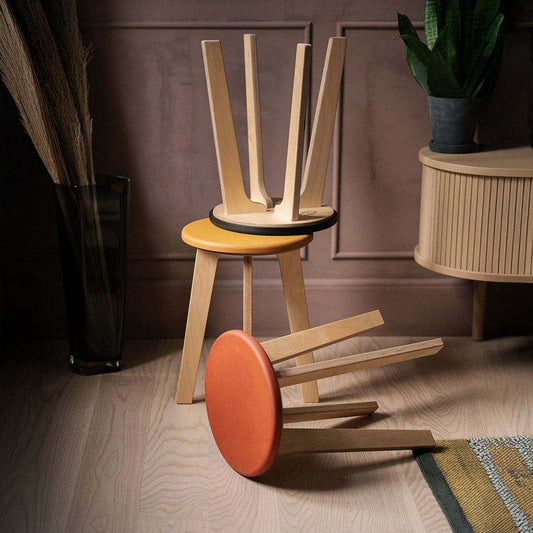 Three colourful Bjørk stools in orange, black and yellow Valchromat with birch plywood legs in a modern interior