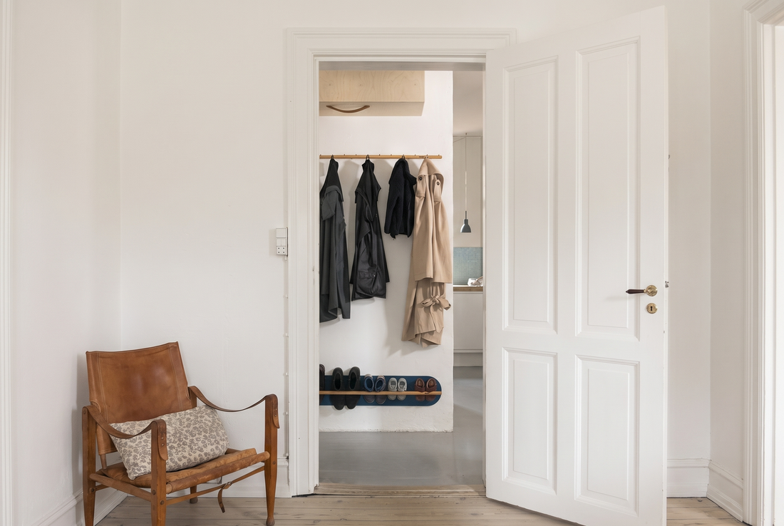 Small Copenhagen entryway with a wall-mounted shoe rack, coats on a peg rail, and a clear floor