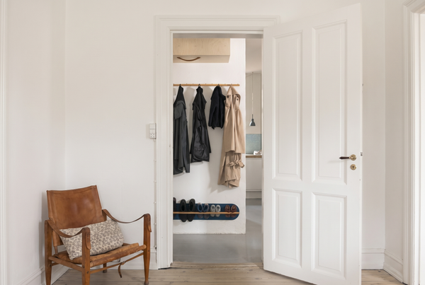 Small Copenhagen entryway with a wall-mounted shoe rack, coats on a peg rail, and a clear floor