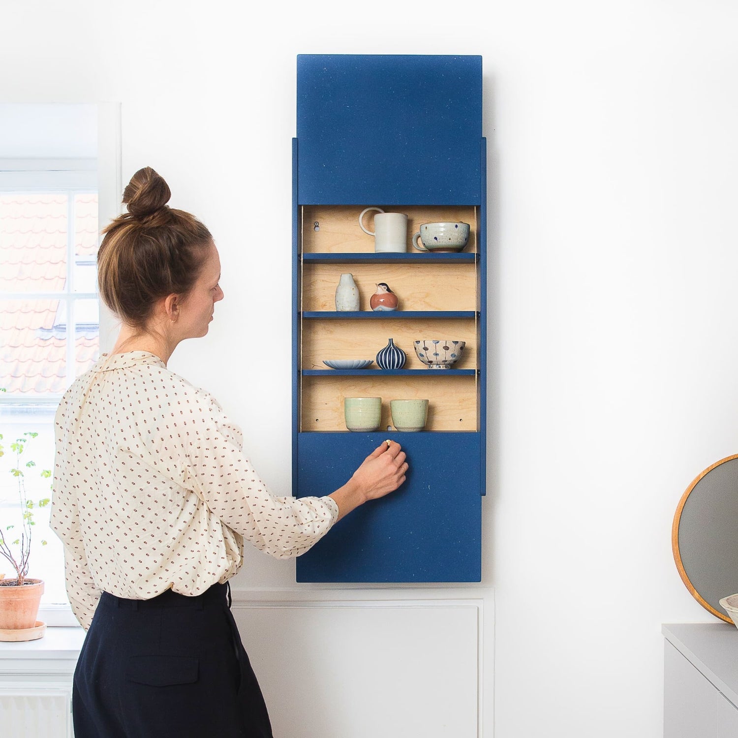 Woman reaching into the open Balance wall cabinet in blue Valchromat® in a modern kitchen