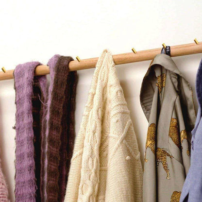Wall-mounted coat rack "Adapt" in solid oak with brass hooks, displaying scarves and garments.