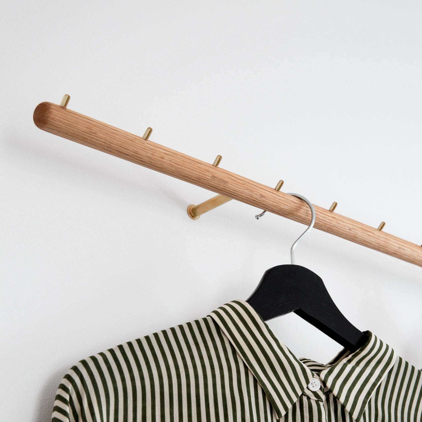 Wall-mounted oak coat rack with brass hooks and striped shirt.