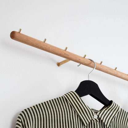 Wall-mounted oak coat rack with brass hooks and striped shirt.