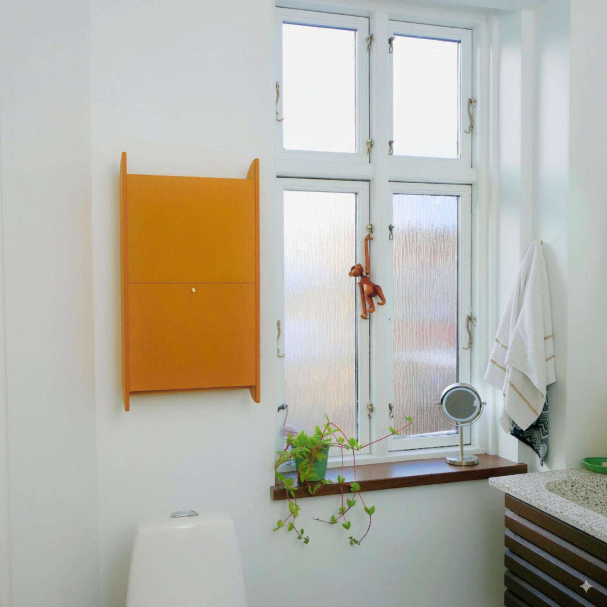 Wall-mounted yellow space-saving cabinet "Balance" in a modern bathroom with window and small shelf decor