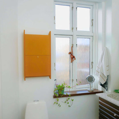 Wall-mounted yellow space-saving cabinet "Balance" in a modern bathroom with window and small shelf decor