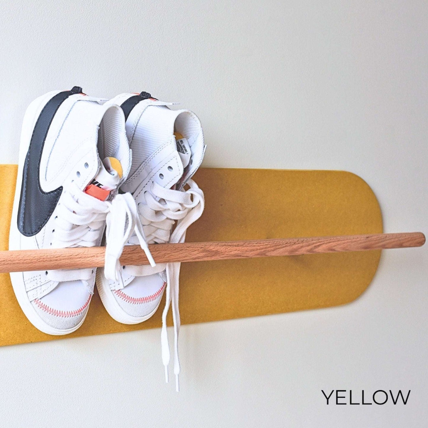 White Nike sneakers on a wooden Shoe  Shelf with yellow wall protector against a white wall.