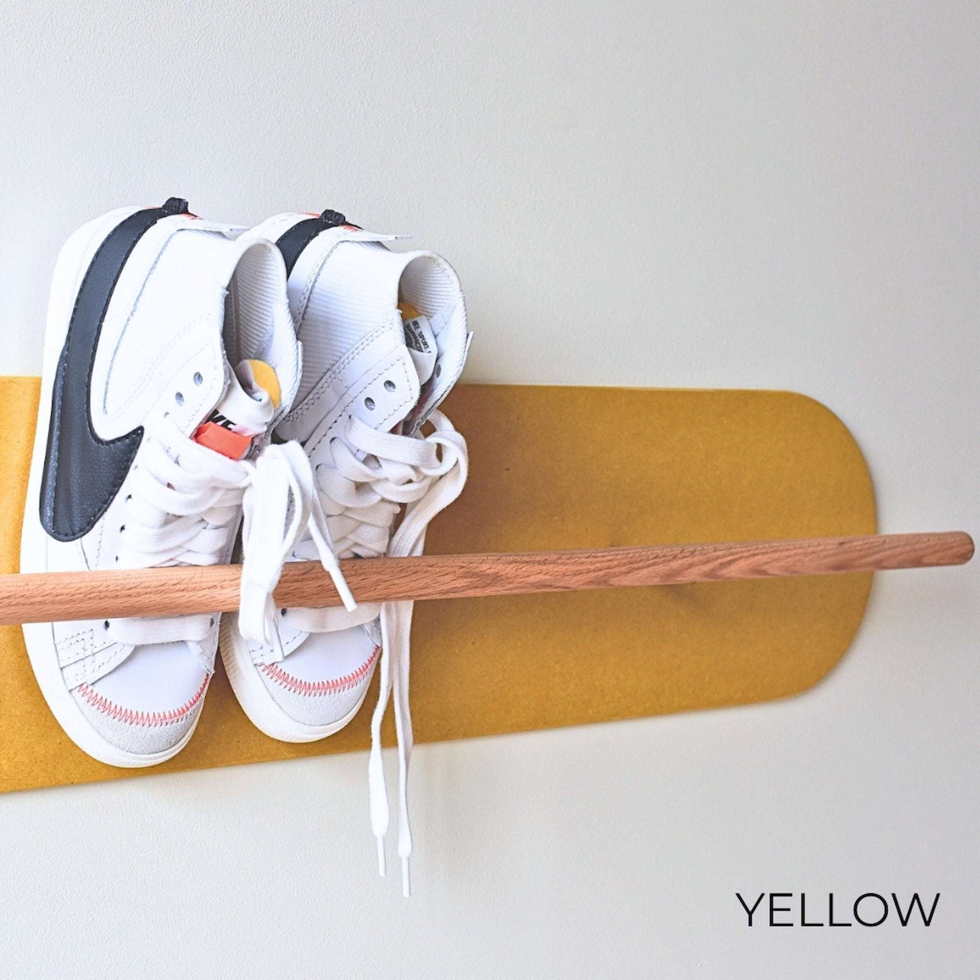 White Nike sneakers on a wooden Shoe  Shelf with yellow wall protector against a white wall.