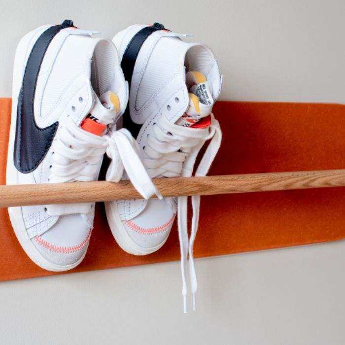 space saving shoe rack with solid oak rod and orange wall protector holding white sneakers in hallway