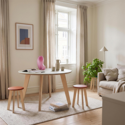 Round Bjørk dining table with birch plywood legs and two Bjørk stools with orange seats in a bright living room