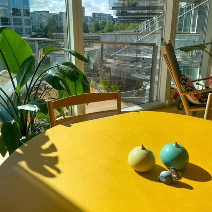 Birch dining table with vibrant yellow Valchromat top in a bright room with plants and balcony view