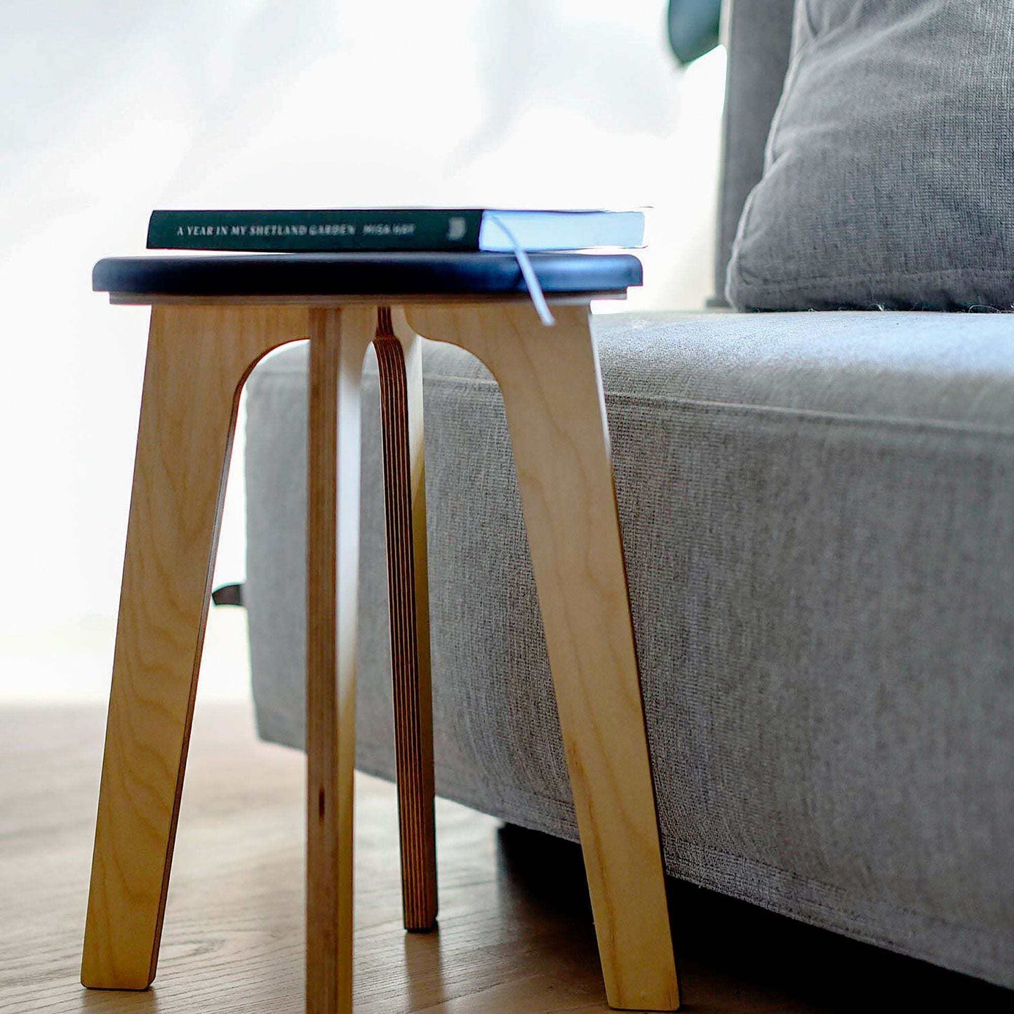 Minimalist birch stool with vibrant Valchromat seat next to a gray sofa in a modern living room