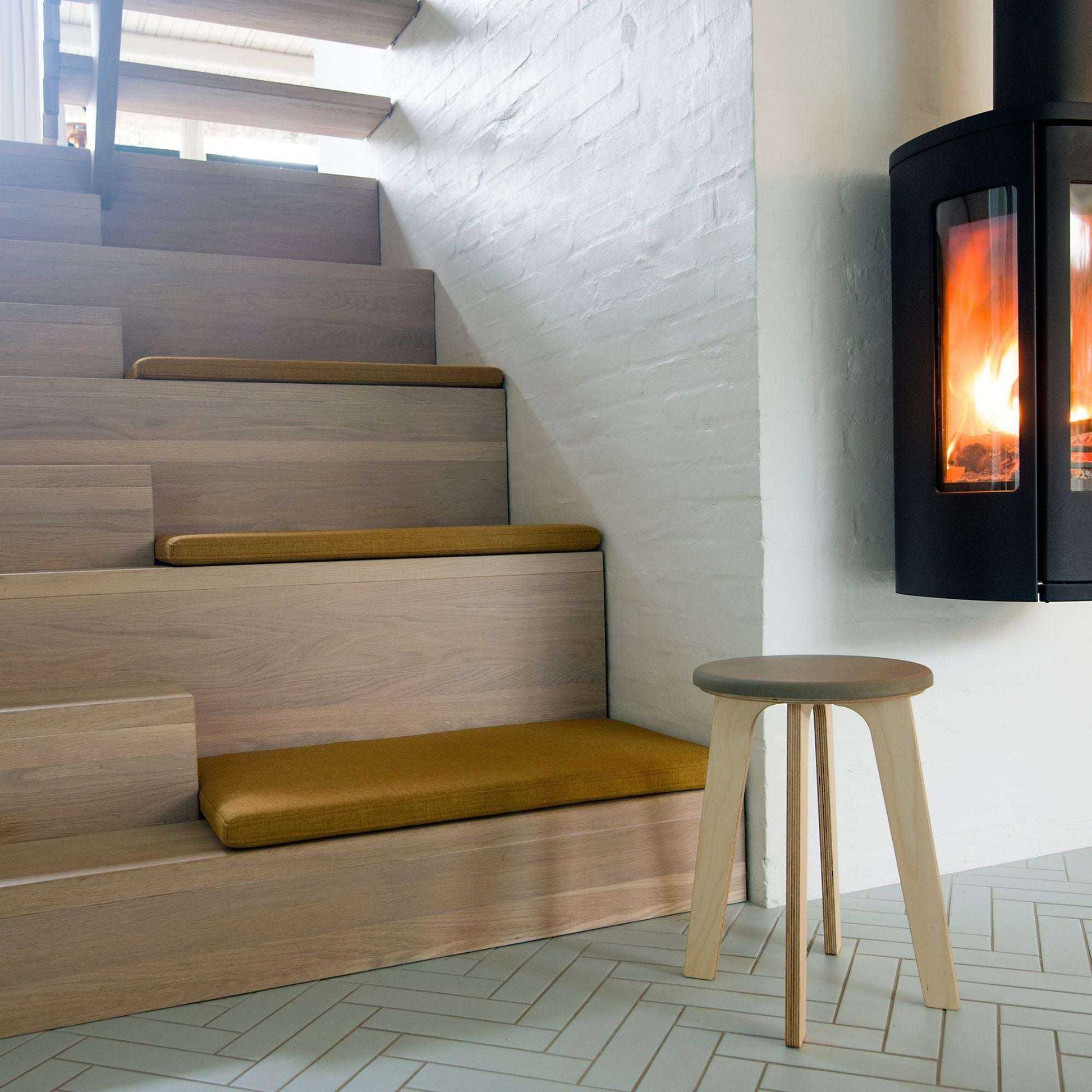 Minimalist birch stool named Bjørk next to modern fireplace and wooden stairs with cushions