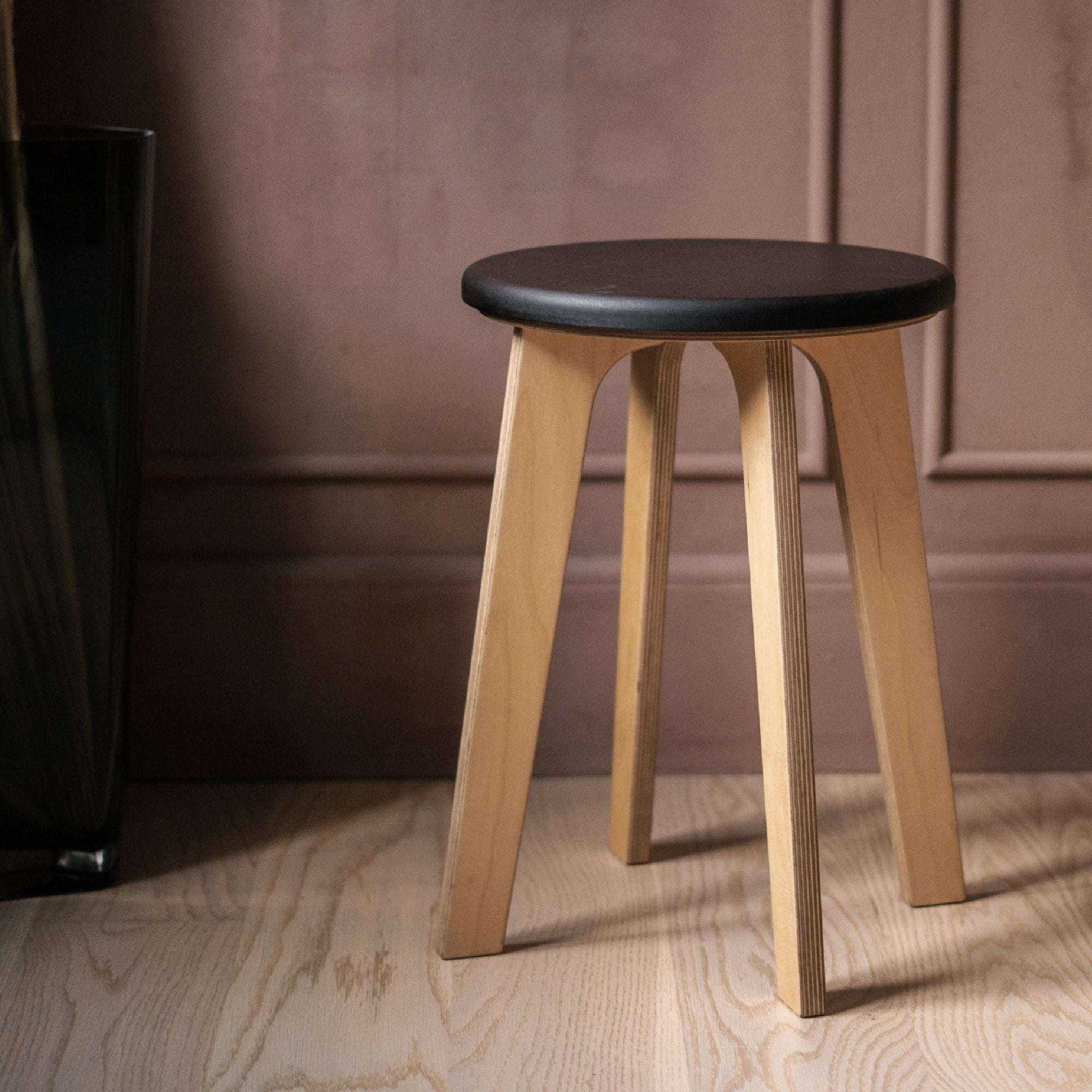 Minimalist birch stool with natural wood legs and dark round seat in modern interior