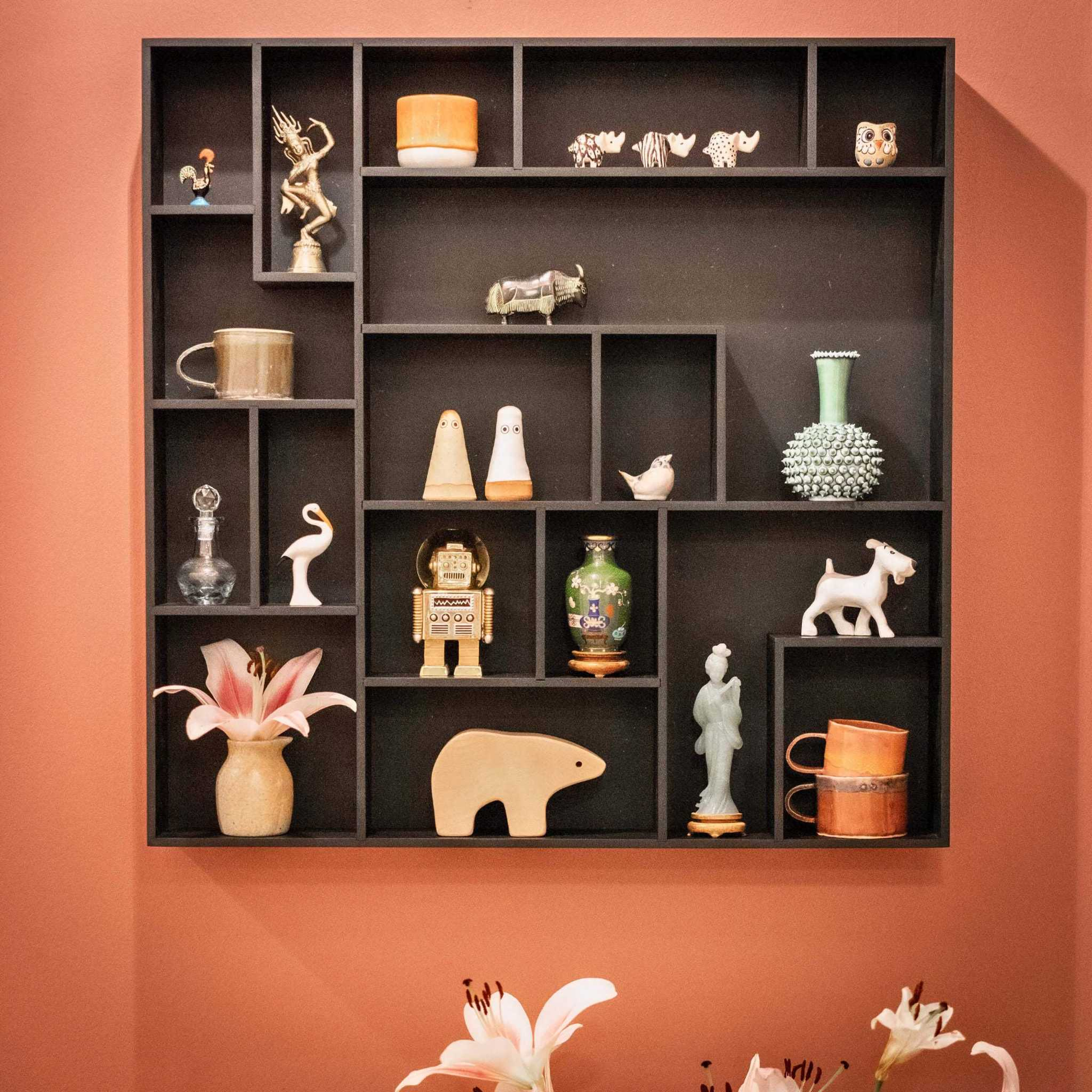 NicNac Timeless Box Shelf in black, wall-mounted on a terracotta wall and styled with small collectibles and flowers