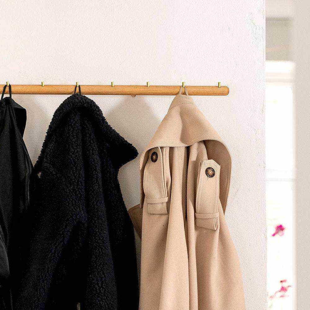 Wall-mounted oak coat rack with brass hooks, holding coats.