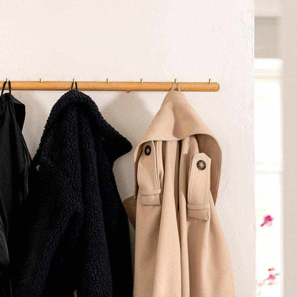 Wall-mounted oak coat rack with brass hooks, holding coats.